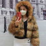 Furry winter coat with hood, woman taking selfie in snowy city street.