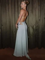 Woman in elegant backless gown standing against wooden backdrop.