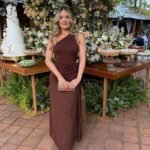 Woman in brown dress standing outdoors with floral arrangements and dessert table.