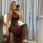Woman in brown jumpsuit taking mirror selfie in fitting room.