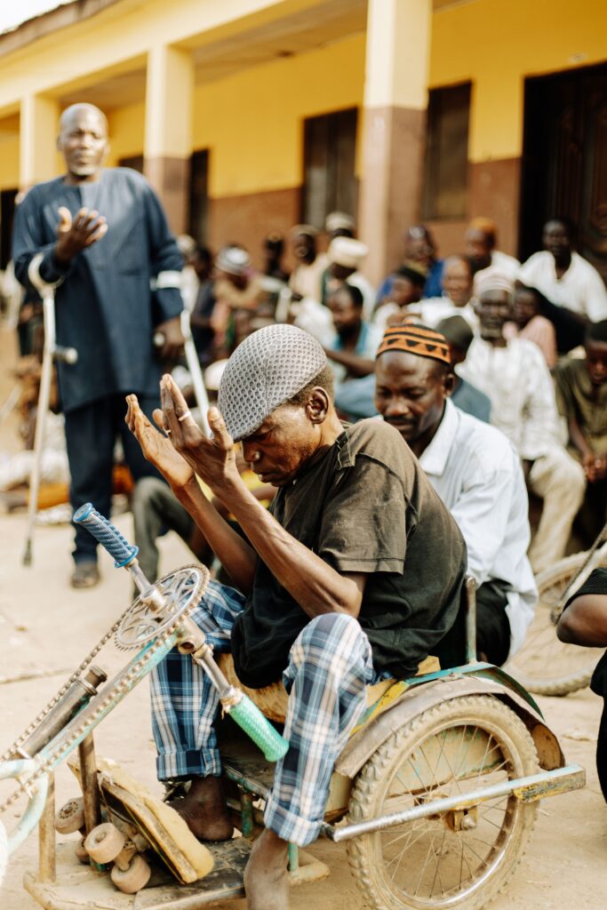 A child on crutches stands among a crowd of people gathered outdoors